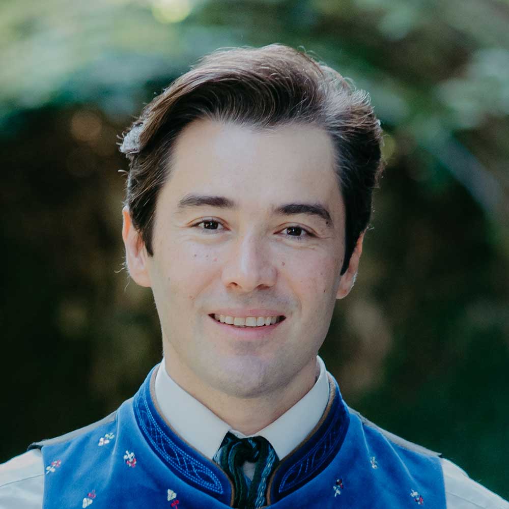 Portrait of Dmitry Iogman, an internationally acclaimed tenor, smiling confidently in a sophisticated setting.