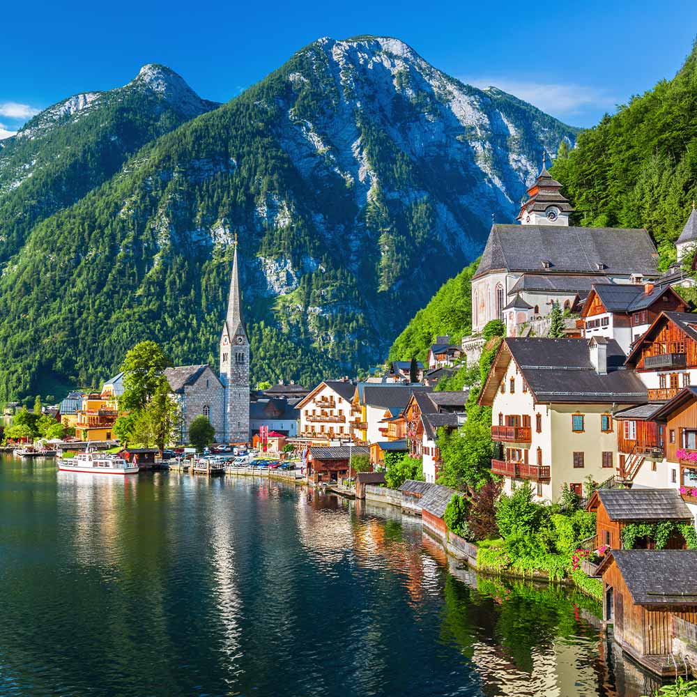 A scenic summer view of Hallstatt from the water, showcasing the village’s iconic skyline, wooden architecture, and alpine backdrop.