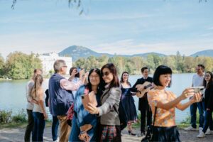 Tourists gather by the lake opposite Schloss Leopoldskron, enjoying the unrivaled view of the palace with its reflection on the water's surface, a popular photo spot commemorating the setting of a classic musical story.