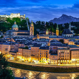 Salzburg by night with its illuminated skyline and the Bavarian Alps in the background.