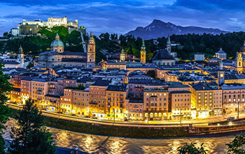 Night view of Salzburg’s illuminated skyline with the Bavarian Alps in the background, optimized for desktop viewing.