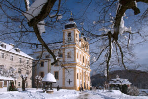 Left-side view of Maria Plain pilgrimage church in winter, framed by a snow-covered tree.