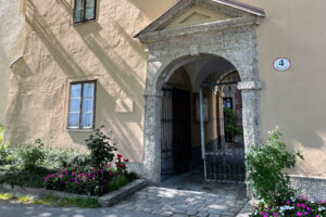 A stone gateway adorned with wrought-iron details leads to the historic Nonnberg Abbey, surrounded by flourishing pink and red flowers under the shadow of the majestic Alps.