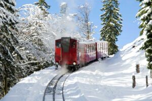 The Advent Train traveling through a snowy landscape on Schafberg during the day.