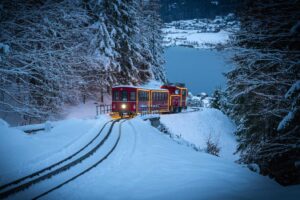 The Advent Train traveling up Schafberg in the evening, with snowy Lake Wolfgang visible in the background.