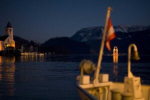 Ship approaching St. Wolfgang at night with a distant lantern illuminating the scene.