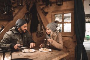 Couple inside a cozy hut at St. Wolfgang Christmas Market, enjoying wine and Austrian traditional dishes.