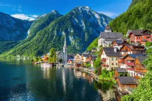 A summer view of Hallstatt from the water, featuring the iconic church in the center and the majestic alpine mountains in the background.