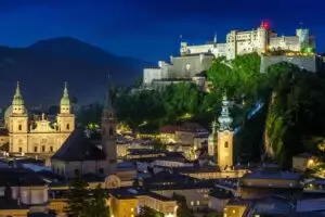 Nighttime view of Salzburg’s Old Town from Mönchsberg, with the Hohensalzburg Fortress, Cathedral, and St. Peter’s Abbey illuminated.